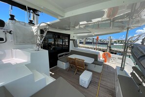 Le pont d’un bateau, avec un espace salon, une table et une glacière.