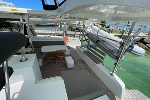 Un pont de bateau aménagé avec des sièges, une table et une vue sur le port de plaisance.