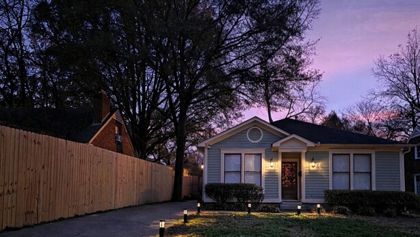 A residential house with a front yard, a wooden fence, and two outdoor lights.