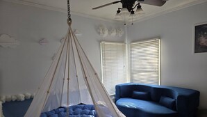 A room with a hanging canopy bed, a blue sofa, and a ceiling fan.
