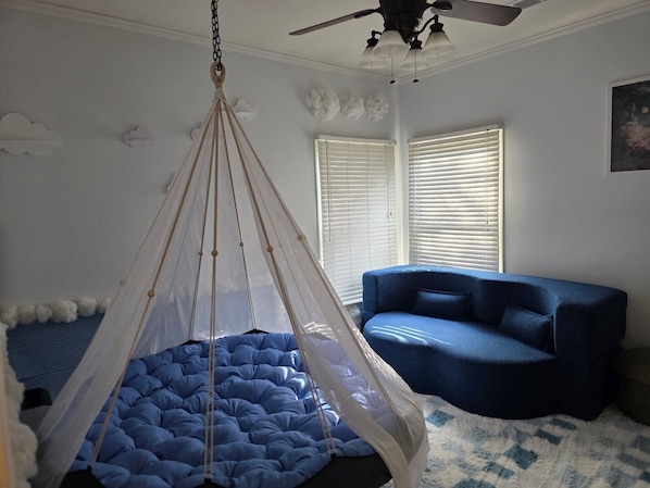 A room with a hanging canopy bed, a blue sofa, and a ceiling fan.