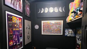 A room with a black wall, a green couch, a framed poster, a framed painting, and a shelf with plush toys.