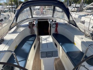 A boat's deck with two seating areas, a steering wheel, and a netted railing.