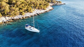 Un velero anclado cerca de una costa rocosa con árboles densos.