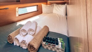 A compact, well-lit cabin with a bed, neatly rolled towels, and a small shelf with toiletries. - Sun-Kissed Sailing Adventure in Islas Sarónicas (Alimos)