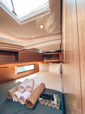 Ein gemütliches, helles Kabinett mit einem Bett, ordentlich aufgerollten Handtüchern und einem kleinen Regal mit Toilettenartikeln.