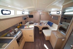 A compact galley with a stove, sink, and a small seating area with cushions. - Sun-Kissed Sailing Adventure in Islas Sarónicas (Alimos)