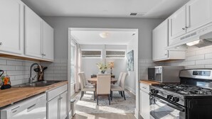 A modern kitchen with white cabinetry, a wooden countertop, a dining table with chairs, a stove, and a microwave. - Historic Wilmington Estate, 5BR/3 Suites - Riverwalk, VIP Parking (Wilmington)