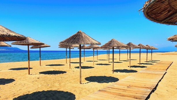 Ein Strand mit Holzstegen und Reetdachschirmen.