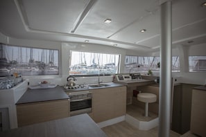 Eine moderne Küche mit einer zentralen Kochinsel, einem Herd und einem Spülbecken. Große Fenster bieten Blick auf den Yachthafen.