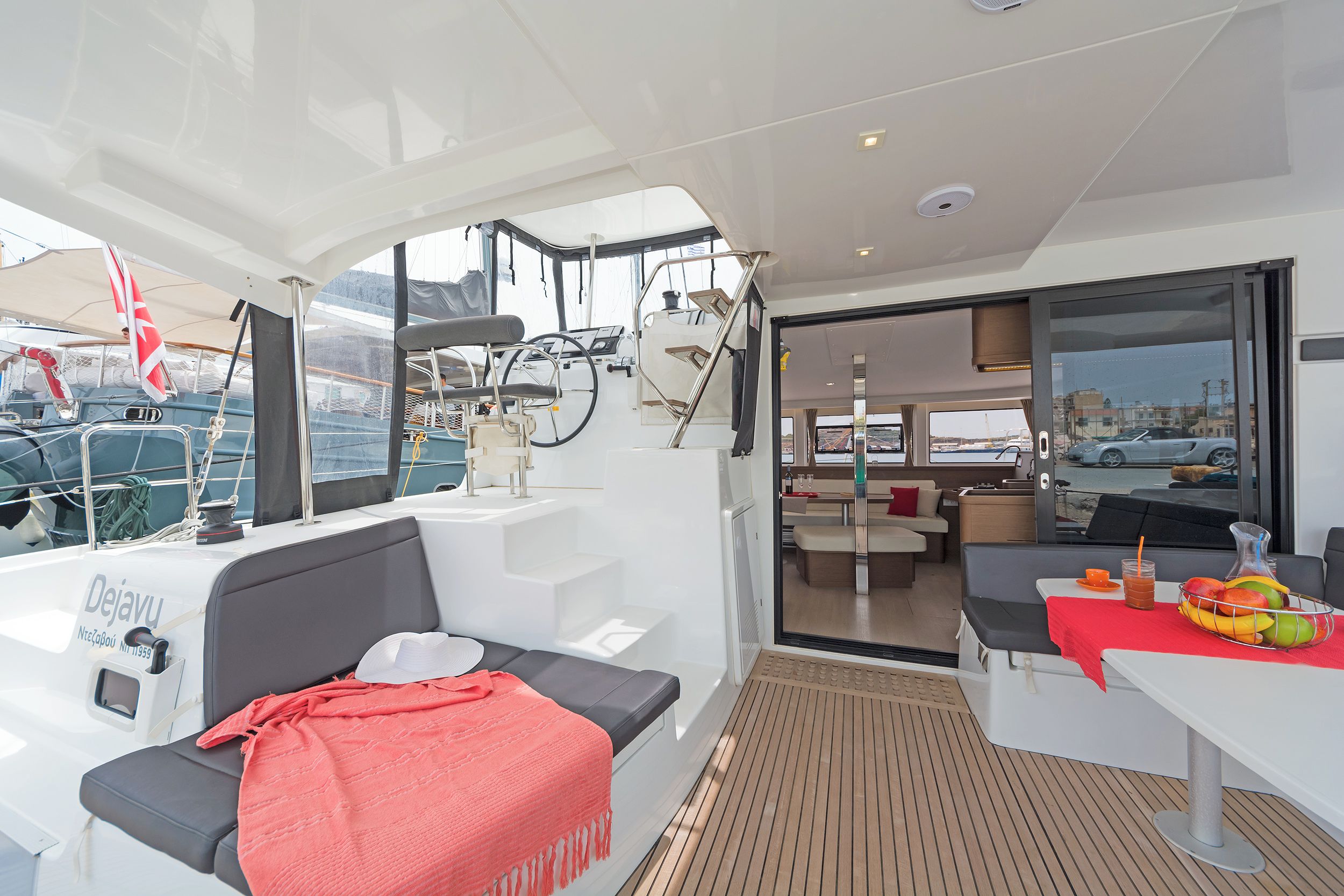 L'intérieur d'un yacht, avec un coin salon, une table à manger décorée de fruits et une vue sur le port de plaisance.