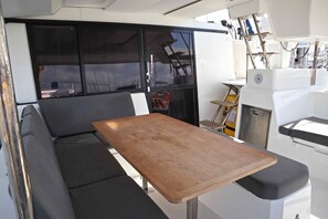 A compact interior with a wooden table, a cushioned bench, and a window with a view. - Sun-Kissed Sailing Adventure in Islas Sarónicas (Alimos)