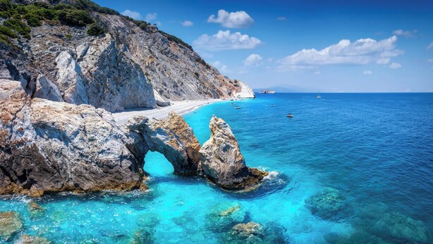 Paisagem costeira com um penhasco rochoso, águas turquesa cristalinas e uma formação rochosa em arco natural.