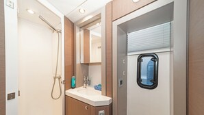 A bathroom with a shower, sink, mirror, and window.
