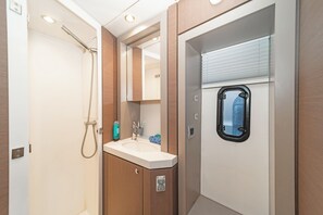 Baño con ducha, lavamanos, espejo y ventana.