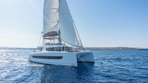 A white catamaran with 'BALI' written on the sail and hull, sailing on calm waters.