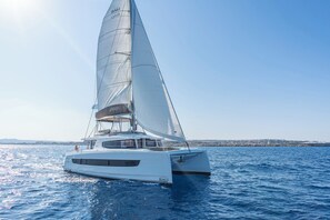 A white catamaran with 'BALI' written on the sail and hull, sailing on calm waters.