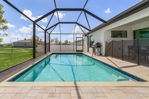 Une piscine rectangulaire à l’eau d’un bleu limpide, entourée d’une zone abritée dotée d’une structure métallique et de murs en verre.