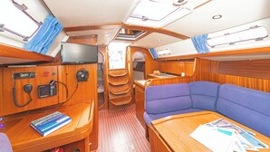 Un interior compacto con un tocador de madera, una zona de estar con cojines azules, una pequeña mesa con papeles y un televisor montado en la pared.