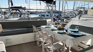 Comedor en un barco con una mesa dispuesta para cuatro personas, rodeada de sillas, y una vista de otros barcos al fondo.