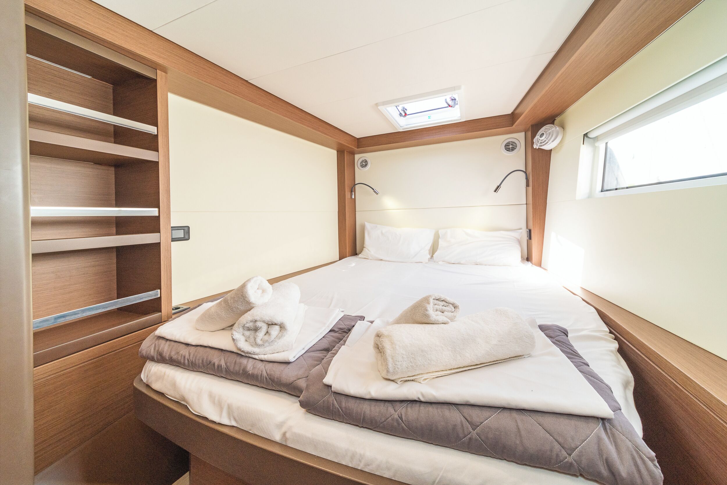 A double bed with two pillows, a bedside table, a built-in shelf, and a window.