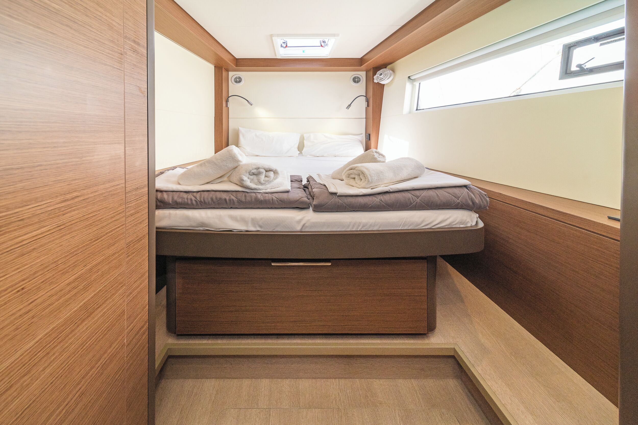 Een compacte, goed verlichte kamer met een bed, opbergladen en een raam.