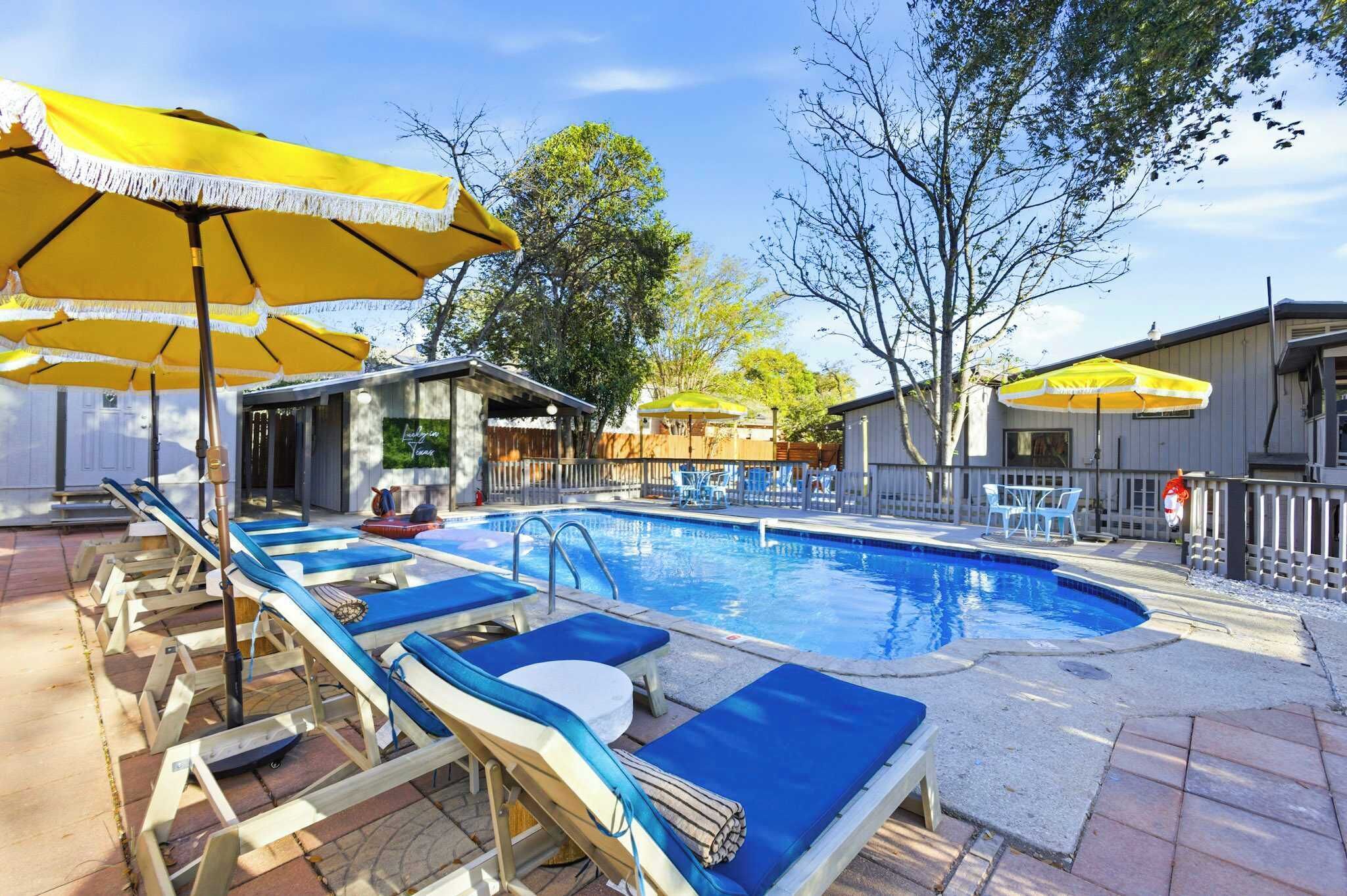 A swimming pool with lounge chairs and yellow umbrellas, surrounded by a fenced area with trees.