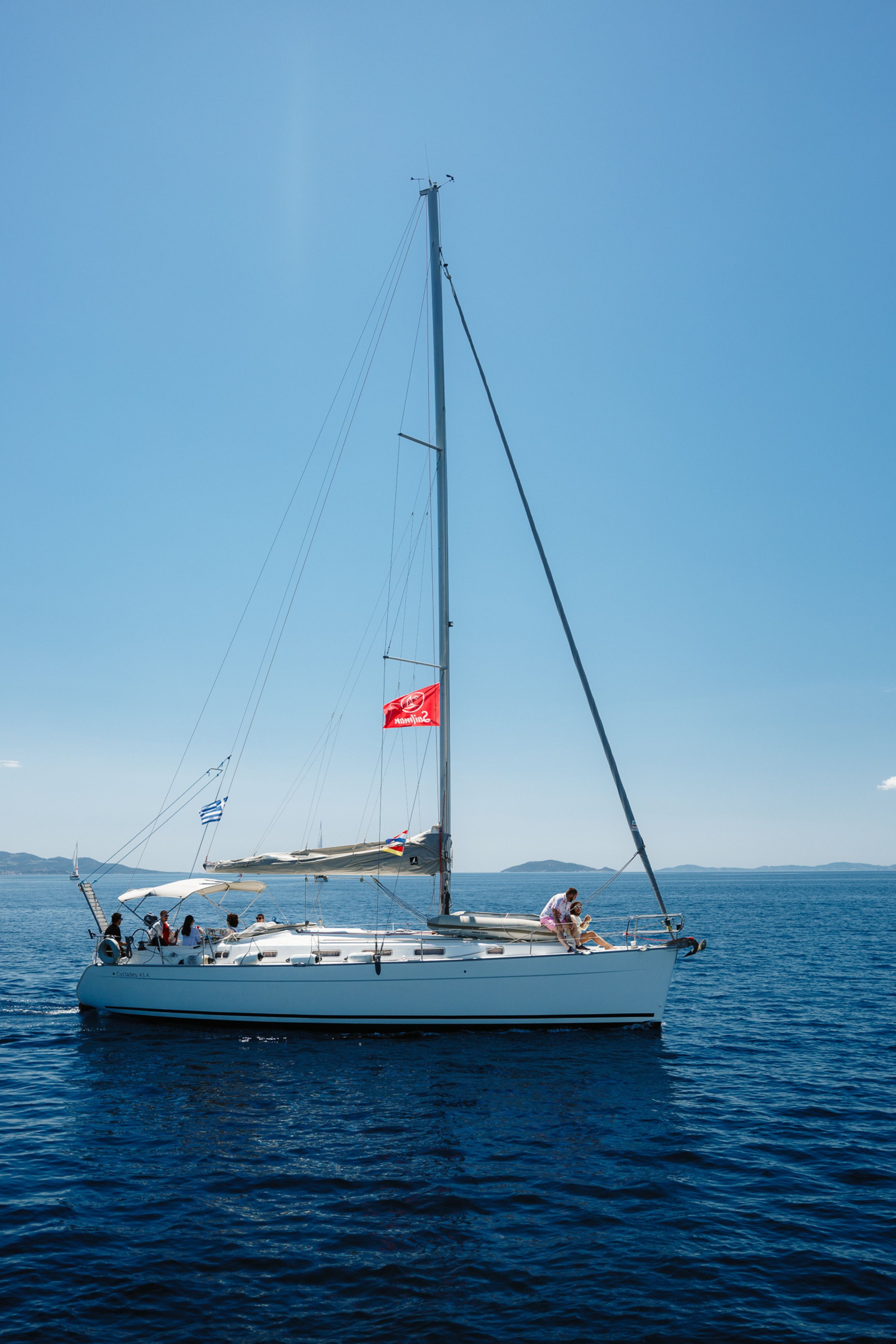 A sailboat with multiple people on board, sailing on a calm sea.