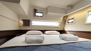 Un lit avec une couette bleue, des oreillers blancs et des serviettes enroulées. Il y a deux petites fenêtres avec des rideaux.