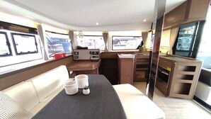 Un intérieur compact et bien éclairé, comprenant un canapé, une petite table agrémentée d’objets décoratifs, une kitchenette et une grande fenêtre offrant une vue sur l’extérieur.