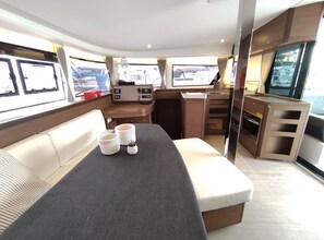 Un intérieur compact et bien éclairé, comprenant un canapé, une petite table agrémentée d’objets décoratifs, une kitchenette et une grande fenêtre offrant une vue sur l’extérieur.