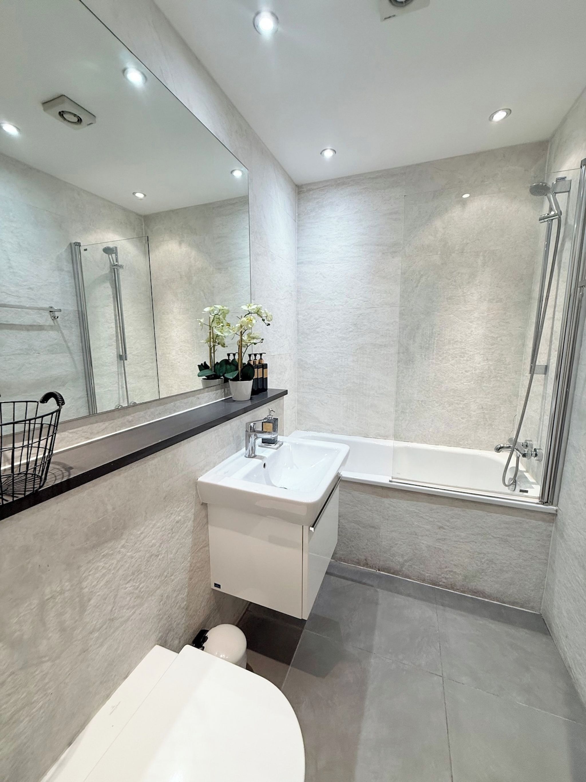 A modern bathroom with a glass-enclosed shower, a white sink, and a toilet.