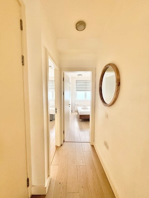 Ein Flur, der in ein Schlafzimmer mit Holzboden, weißen Wänden und einem runden Spiegel führt.