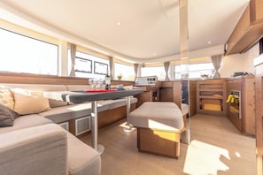 A compact living space with a sofa, a small table, a kitchenette, and a window providing natural light. - Sun-Kissed Sailing Adventure in Islas Sarónicas (Alimos)