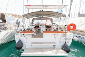 Eine Segelyacht liegt in einer Marina festgemacht, mit einer überdachten Deckfläche, Sitzgelegenheiten und einem Rettungsring.