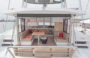 Le pont d’un yacht, aménagé avec un espace repas, des sièges et offrant une vue sur le port de plaisance.