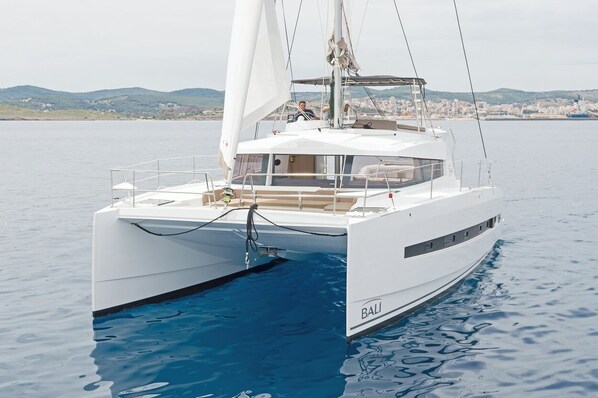 Un catamaran blanc, avec le mot «BALI» écrit sur le côté, est amarré dans des eaux calmes, avec une vue sur la ville en arrière-plan.