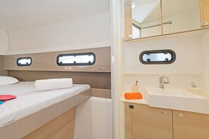 Un intérieur de camping-car compact comprenant un lit, une petite salle de bain avec un lavabo et un miroir, et deux fenêtres.