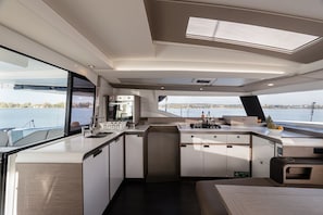 A modern kitchen with a large island, a built-in stove, and a view of the water. - Sun-kissed Sailing Adventure in the Ionian Islands (Preveza)