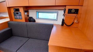 A compact interior with a grey sofa, a small table, and a control panel with a screen. - Sun-Kissed Sailing Adventure in the Ionian Islands, Lefkada (Lefkada)