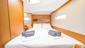 Ein Einzelbett mit weißer Bettwäsche, zwei Handtücher, ein Hut und ein Kopfteil mit integrierter Beleuchtung.