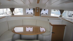 L’intérieur d’un bateau est aménagé avec une table ronde, des sièges rembourrés, un petit coin cuisine et des fenêtres équipées de rideaux.