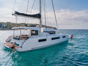 A white yacht with a covered deck, a seating area, and a small table. - Sun-Kissed Sailing Adventure in Islas Sarónicas (Alimos)