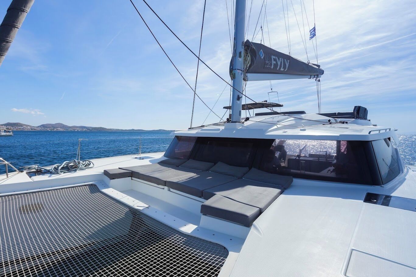 A yacht with a covered deck area, a mast with a flag, and a view of the sea and distant land.
