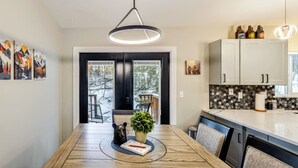 A modern kitchen with white cabinets, a wooden dining table, and a pendant light.