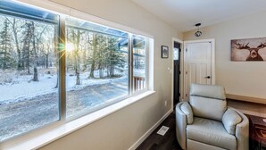 A room with a large window, a chair, a door, and a wall-mounted picture of a deer.