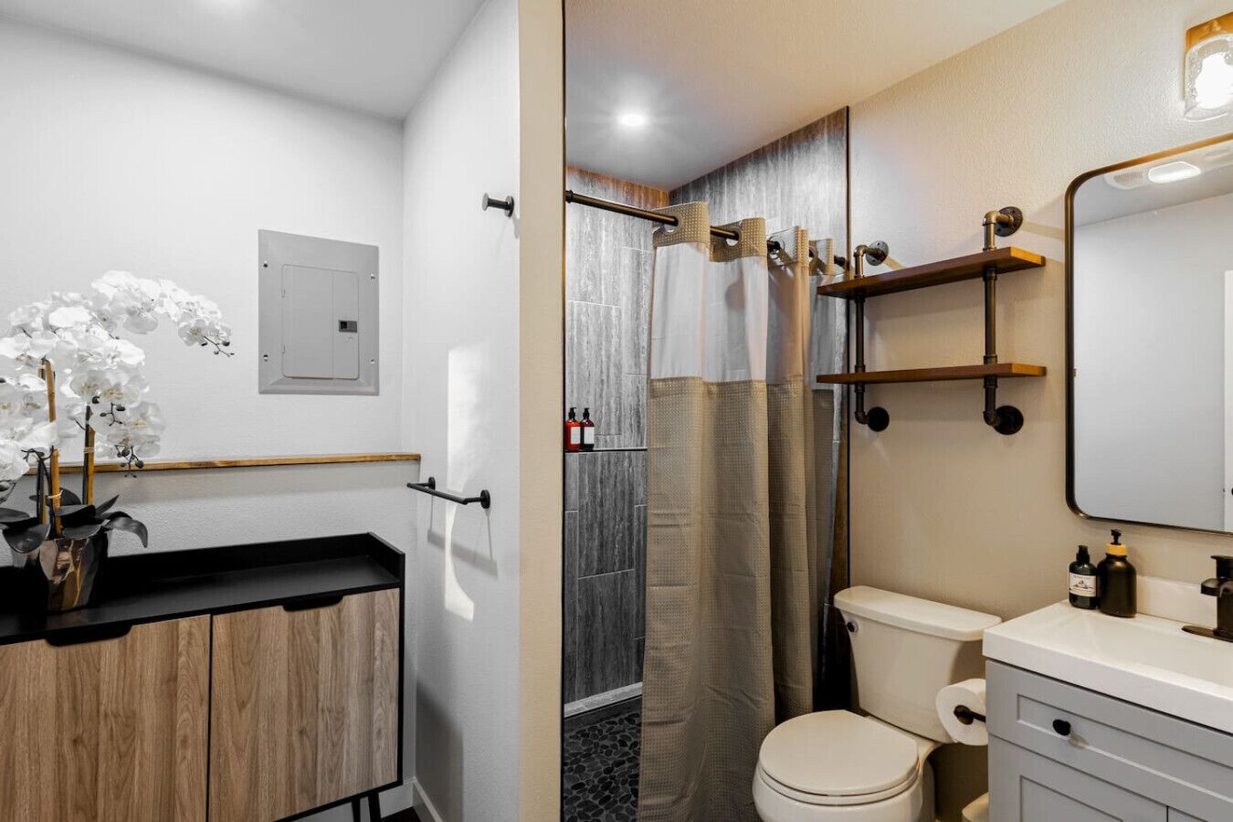 Une salle de bain moderne avec un meuble-lavabo en bois, des toilettes, une douche avec une porte en verre et un miroir.