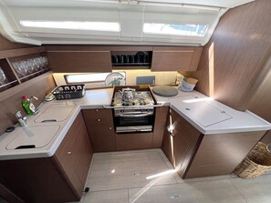 A compact galley kitchen with a stove, oven, and sink, wooden cabinetry, and a small window above the sink. - Sun-Kissed Sailing Adventure in Islas Sarónicas (Alimos)