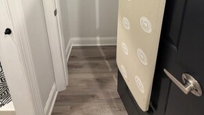 A room with a wooden floor, a door with a towel hanging on it, and a white wall with a coat rack.