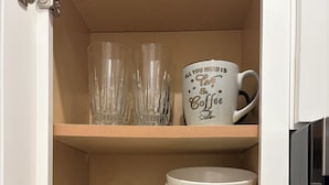 A kitchen cabinet with clear glassware, a coffee mug, and stacked plates.